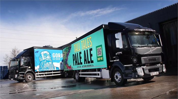 Two Volvo rigid curtainsider trucks with Butcombe Brewery liveries parked outside a distribution centre.