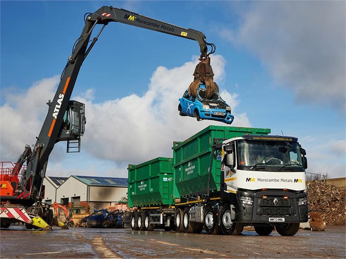 A crane loads a scrap car into a trailer pulled by a Renault Trucks C520 8x4 with a hook loader body in a scrapyard.