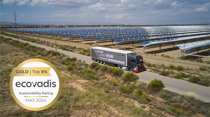 A Man truck driving down a road alongside a solar energy farm with an EcoVadis Sustainability Rating logo affixed.