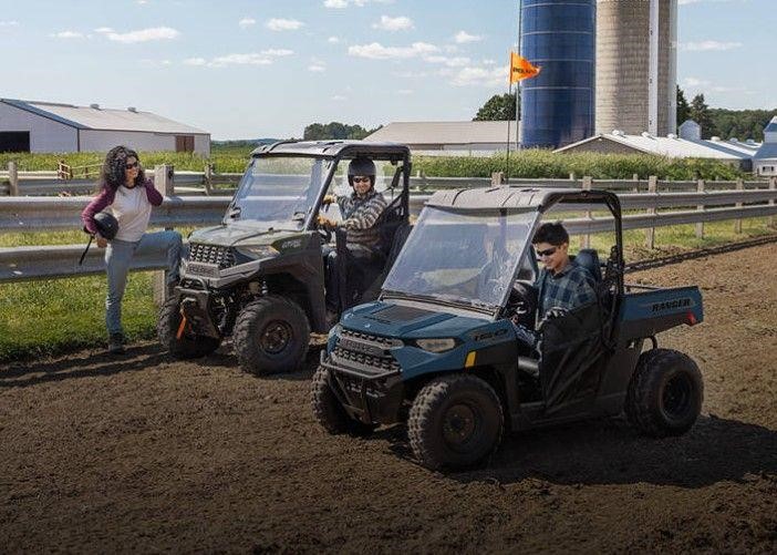 two utvs with drivers parked in front of a white fence