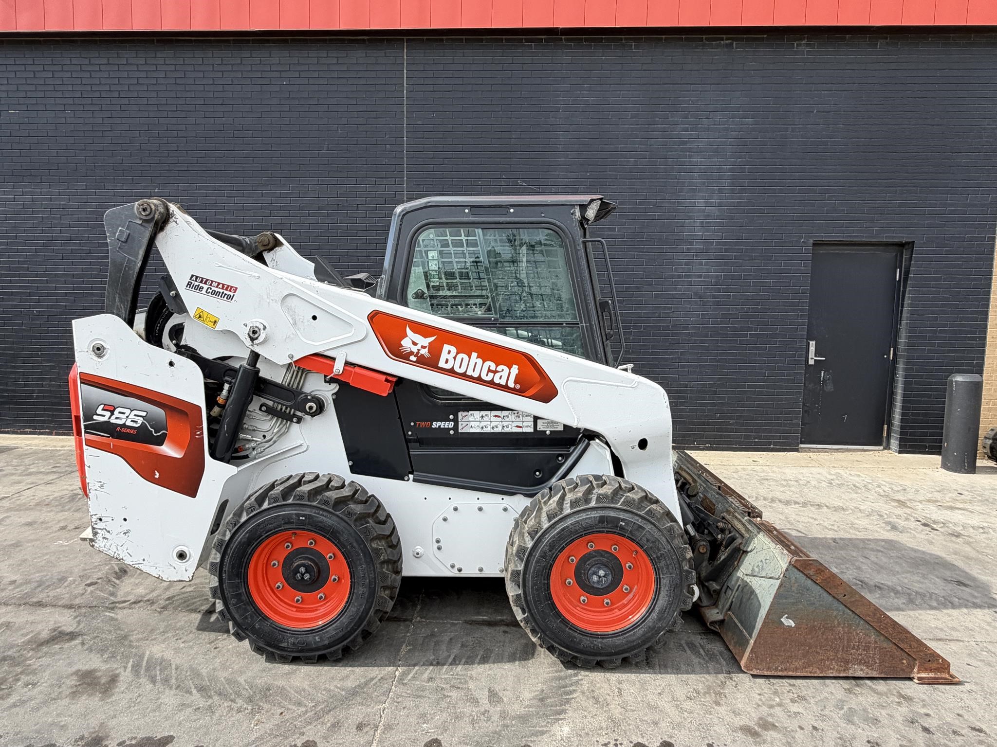 A 2023 Bobcat S86 Wheel Skid Steer sits in front of a building.
