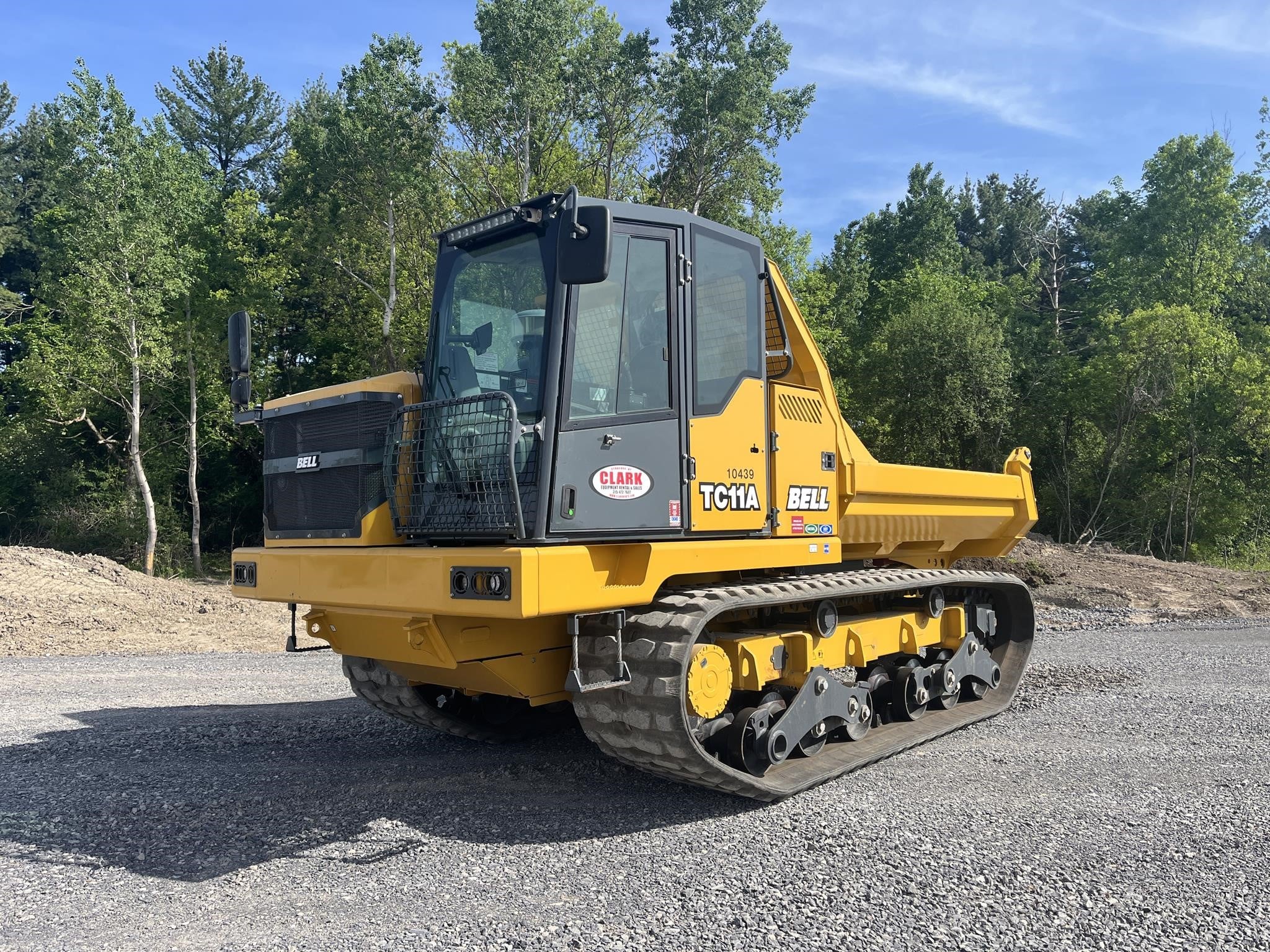 2022 Bell TC11A tracked dumper parked on cement outdoors with trees in the background.