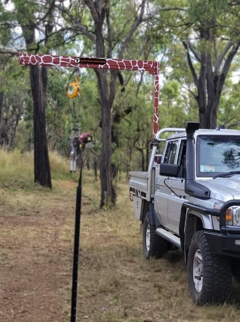 2026 QuikFence Giraffe Picket Driver gantry crane mounted on a utility vehicle in a wooded area.