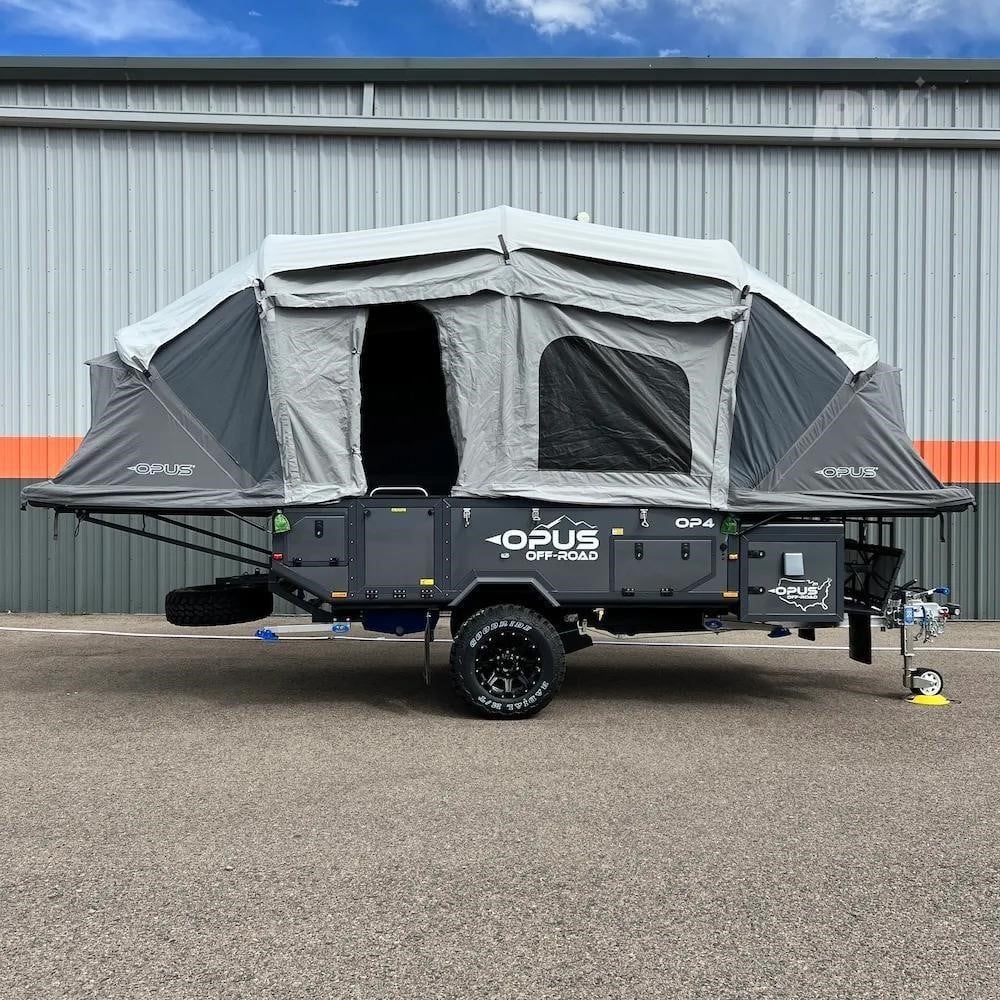 A 2026 Opus Off-Road OP04 soft-sided pop-up camper parked outdoors by a building.