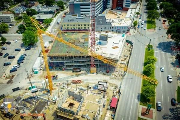 Aerial view of a 2023 Potain IGO T130 tower crane operating at a large construction site surrounded by buildings and streets.