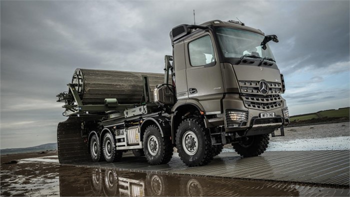 A Mercedes-Benz Arocs sits on a Faun trackway placed over a wet surface.