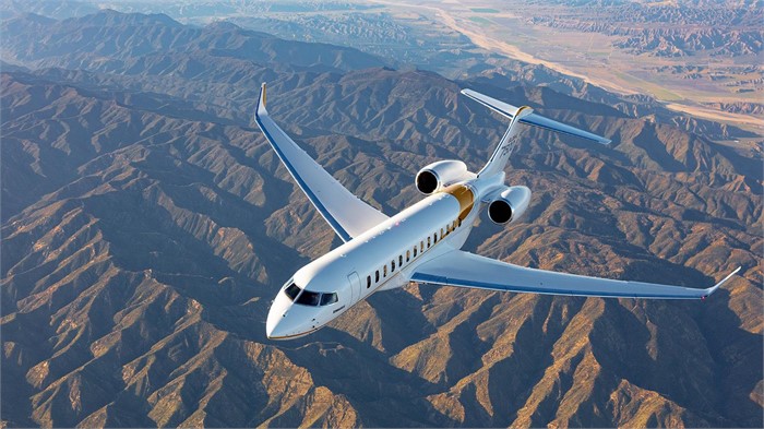 A twin-engine, 19-pasenger white Bombardier Global 7500 executive jet flies over a mountain range during the day.