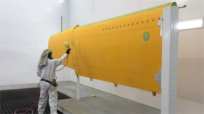 A worker applying yellow-orange paint to a Daher Kodiak turboprop aircraft wing.