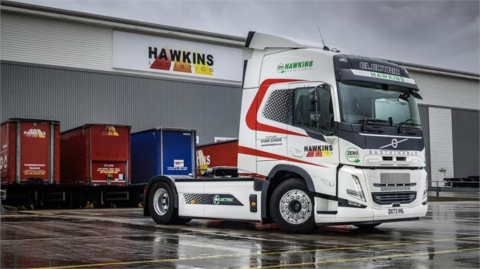 A Volvo FM Electric in Hawkins Logistics’ livery sitting on wet pavement outside the depot.