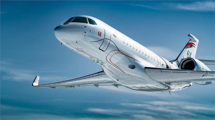 A Dassault Aviation Falcon 6X business jet in flight against a blue sky.