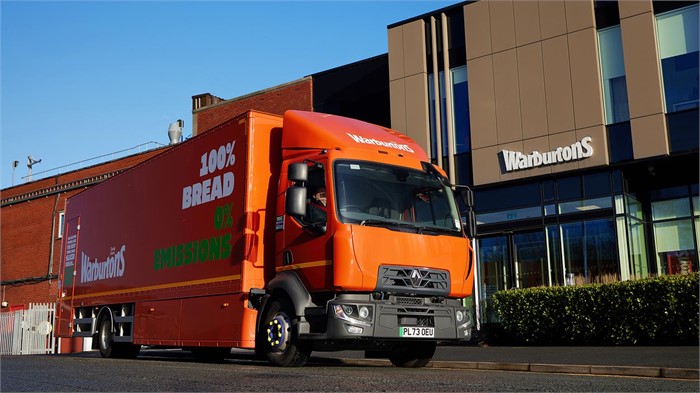 A Renault E-Tech D16 battery-electric truck in Warburtons livery sits outside a Warburtons facility.