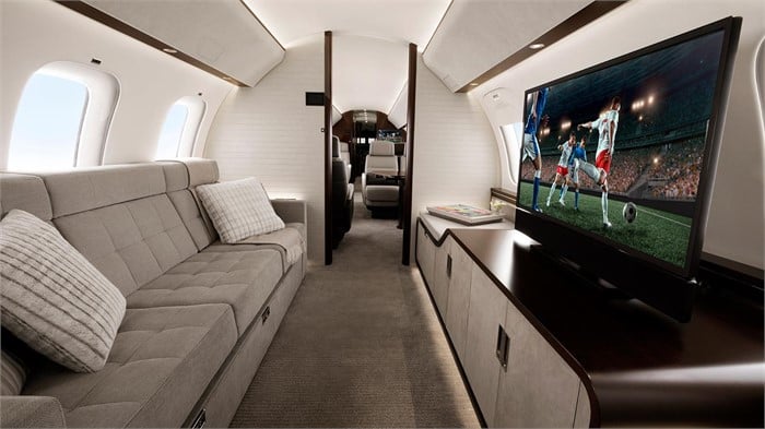 The interior of a Bombardier Global 7500 showing a 3-section divan opposite a 55-inch 4K television.