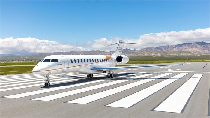 A Bombardier Global 7500 ultra-long-range business jet sits on a tarmac with mountains in the background.
