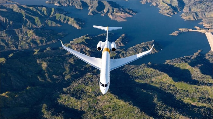 A Bombardier Global 7500 ultra-long-range business jet flies over bodies of water surrounded by mountains.