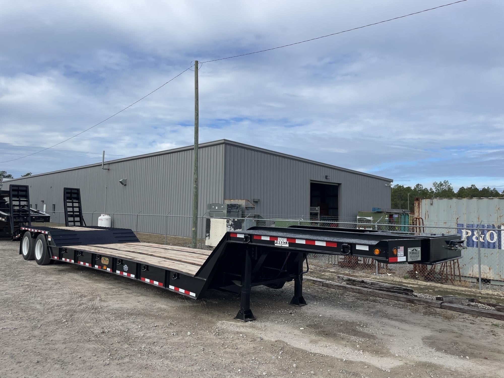 A 2025 McLendon Lowboy semi-trailer sits on a lot.