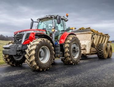 a red tractor pulling a manure spreader down a roadway