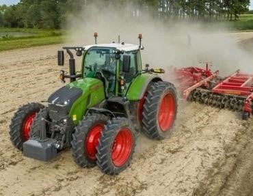 a large green tractor with dual front and rear wheels pulling a tillage disc in a field