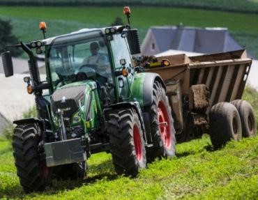 an image of a green tractor with red rims pulling a manure spreader in a field